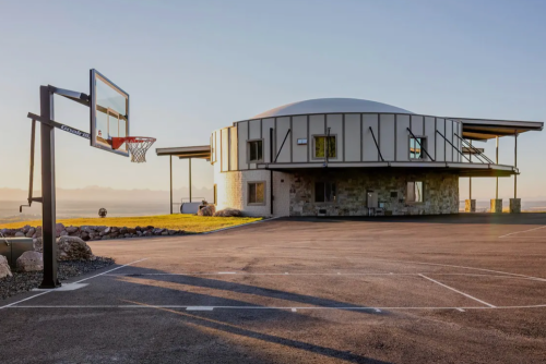 A unique round building beside a basketball hoop on a paved court, set against a clear sky and distant mountains.